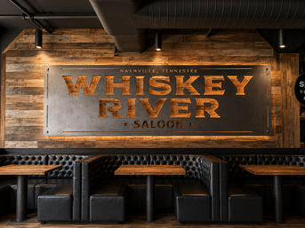 Cozy Nashville, Tennessee saloon interior with a large backlit metal sign on a reclaimed wood wall, tufted black leather booths and rustic wooden tables.