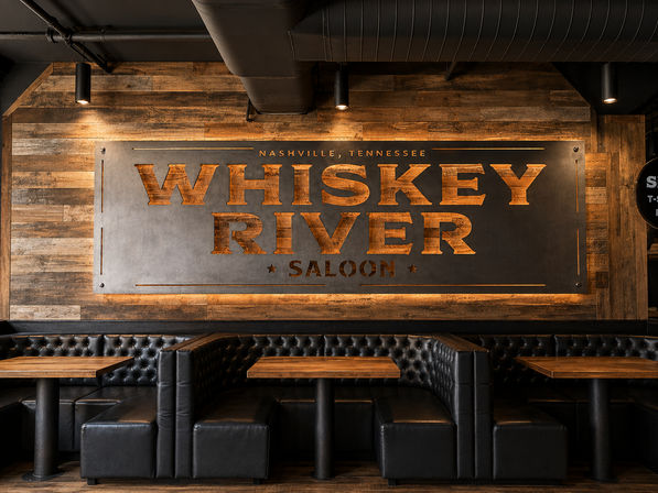 Cozy Nashville, Tennessee saloon interior with a large backlit metal sign on a reclaimed wood wall, tufted black leather booths and rustic wooden tables.