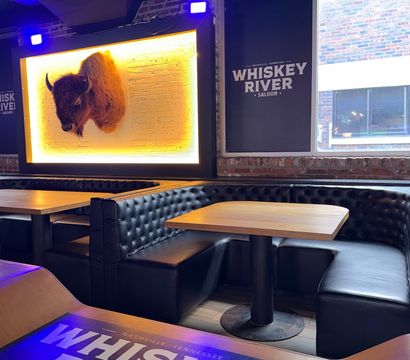 Stylish Nashville bar interior with tufted black leather booths, wooden tables, backlit mounted bison head on exposed brick and blue accent lighting