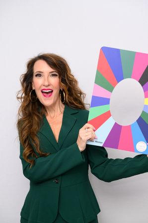 Smiling woman in an emerald green blazer holding a vibrant multicolor color-wheel palette — upbeat studio portrait for color analysis and fashion styling.