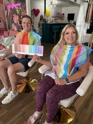 Smiling man and woman in a boutique salon during a color analysis session, wearing bright seasonal drapes and holding a “Light Spring” palette.