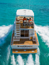 Aerial view of a white motor yacht cruising turquoise Nassau, Bahamas waters with two people at the helm on a teak aft deck, leaving frothy wake trails behind.