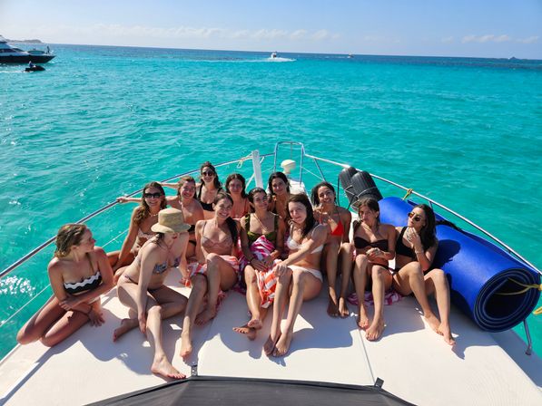 Group of women in swimsuits lounging on the bow of a yacht over vivid turquoise tropical waters under a sunny blue sky