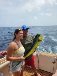 Two smiling anglers on a sportfishing boat holding a bright green-yellow mahi-mahi (dolphinfish) over the open offshore blue ocean — fresh deep-sea catch.