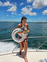 Person in a white swimsuit and heart-shaped sunglasses holding a life ring on a boat in turquoise waters near Nassau, Bahamas under a sunny blue sky.