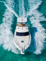 Aerial drone view of a white luxury yacht speeding across clear turquoise tropical water, carving twin foamy wake trails behind it.