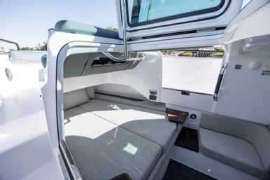 Sunlit modern boat cabin interior with gray V-berth cushions, compact seating nook, open hatch and built-in storage — cozy marine berth for coastal cruising.