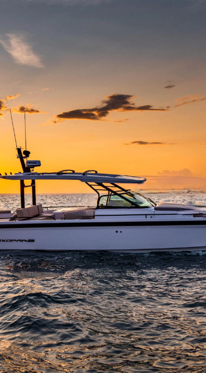 Sleek motorboat gliding across choppy ocean waves at golden sunset with vibrant orange sky and sun reflecting on the water