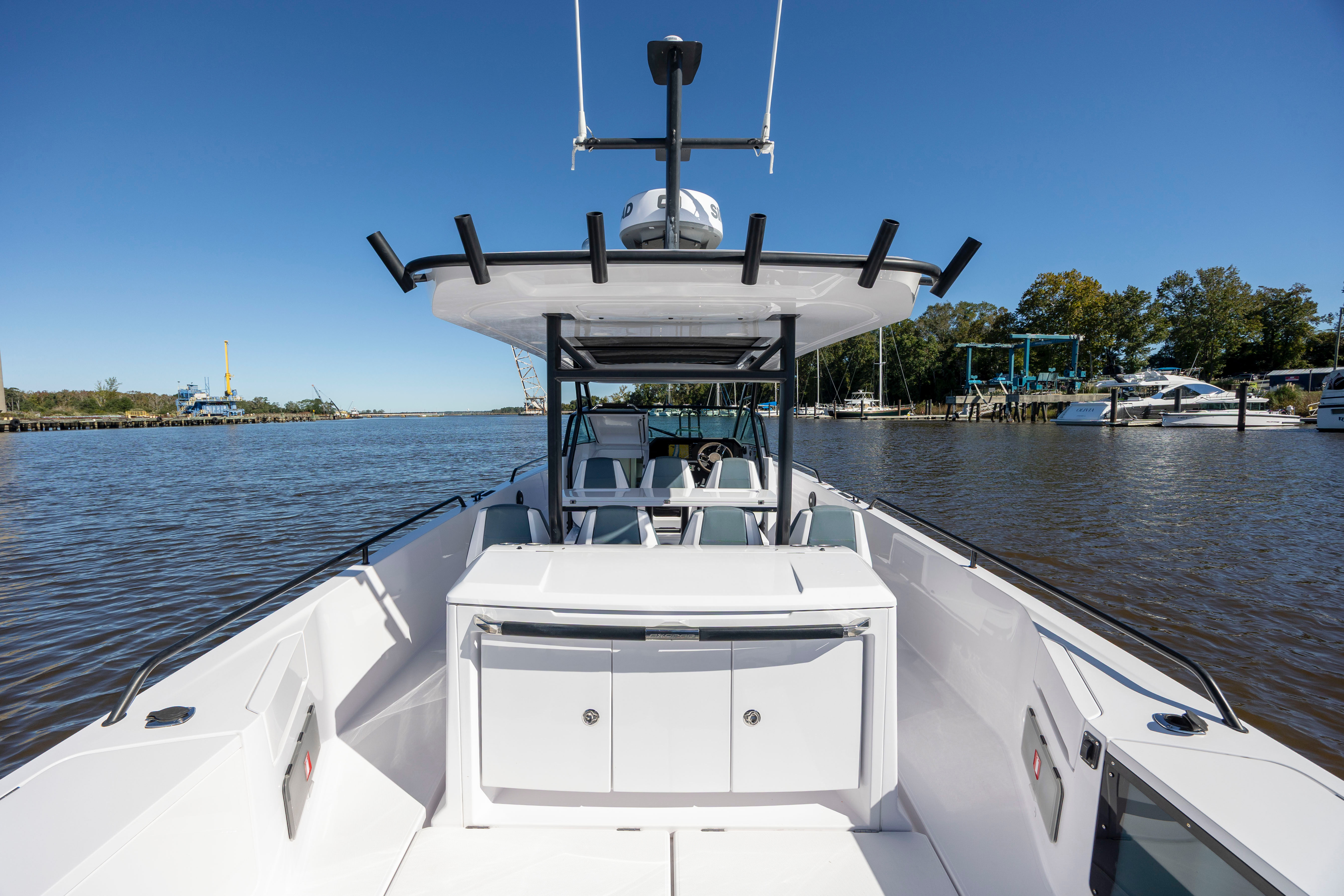 White center-console powerboat with T-top, rod holders, and cushioned helm seating docked at a riverside marina under a bright blue sky