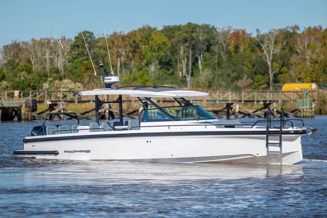 Sleek white dayboat with a hardtop cruising on a calm river past a wooden dock and tree-lined shoreline under a clear blue sky