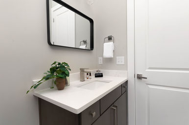 Sleek modern bathroom vanity with white quartz countertop and undermount sink, matte gray cabinets, black-framed mirror, chrome faucet, small potted plant and a neatly hung hand towel in a bright minimalist powder room.