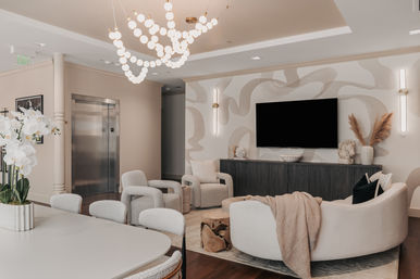 Modern luxury apartment lounge with sculptural globe chandelier, curved cream sofa, cozy boucle armchairs, wall-mounted TV, decorative console and elevator