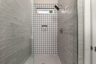 Modern walk-in shower with glass door, gray subway tile walls, geometric circle-pattern accent wall, penny-tile floor, rainfall shower head and narrow horizontal window