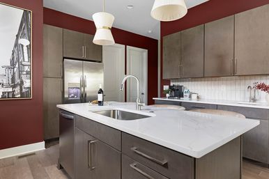 Contemporary kitchen with deep red walls, large white quartz island featuring an undermount sink, stainless steel refrigerator, gray flat-panel cabinets, pendant lights and breakfast seating