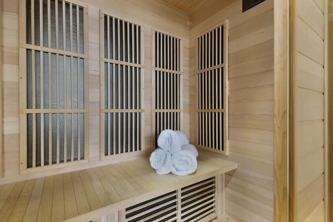 Cozy wood-lined sauna interior with vertical slatted panels and a bench topped by three rolled white towels, modern spa retreat vibe