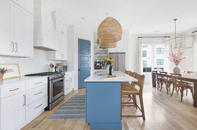 Bright modern farmhouse kitchen with blue island, white shaker cabinets, stainless appliances, rattan pendant lights, wooden bar stools and open-plan dining with hardwood floors