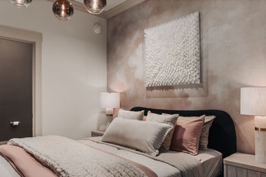 Cozy contemporary bedroom interior with plush cream and blush bedding, black upholstered headboard, matching bedside lamps, textured white sculptural wall art and soft neutral accent wall.