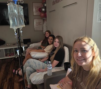 Group of four women relaxing in a cozy wellness lounge receiving IV drip therapy, seated with pillows, water bottle and smiles