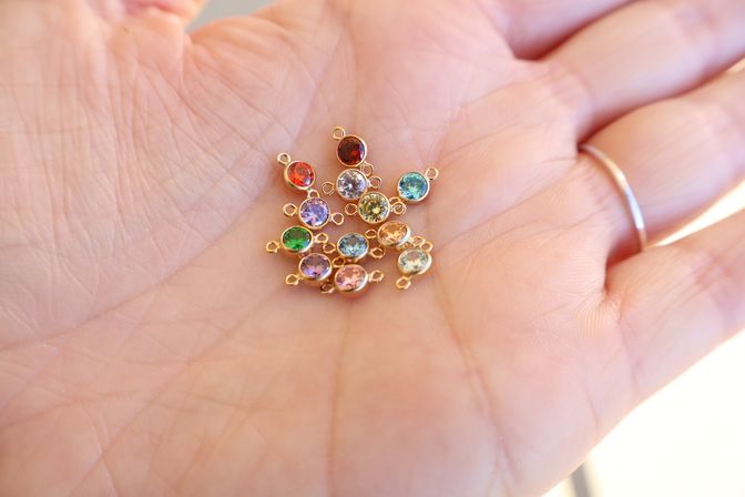 Close-up of a palm holding tiny gold bezel jewelry charms with multicolored faceted crystals in red, green, blue and purple for DIY necklaces and bracelets.