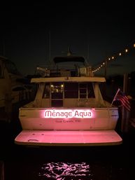 Nighttime motor yacht moored at a Maryland marina with a pink-lit transom sign, string lights along the dock, an American flag, and pink reflections in the water.