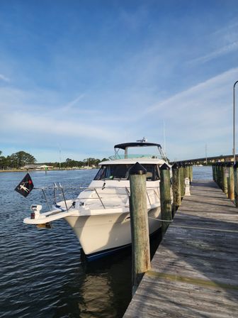 White motor yacht moored to wooden pilings at a sunny marina pier, calm waterfront and clear blue sky