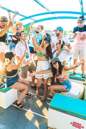 Energetic summer boat party in a marina — people dancing on deck with drinks, sunglasses, and colorful swimwear.