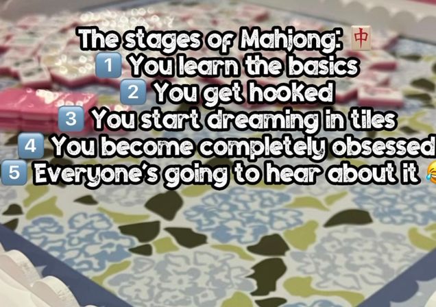Close-up of mahjong tiles on a patterned table with bold overlay text listing the stages of Mahjong: learn the basics, get hooked, dream in tiles, become obsessed, and tell everyone.