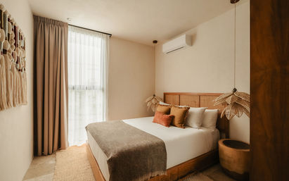 Sunlit modern boho bedroom with a queen bed, woven rattan headboard, earth-tone pillows and throw, hanging wicker pendant lights, sheer floor-to-ceiling curtains and warm wood accents.