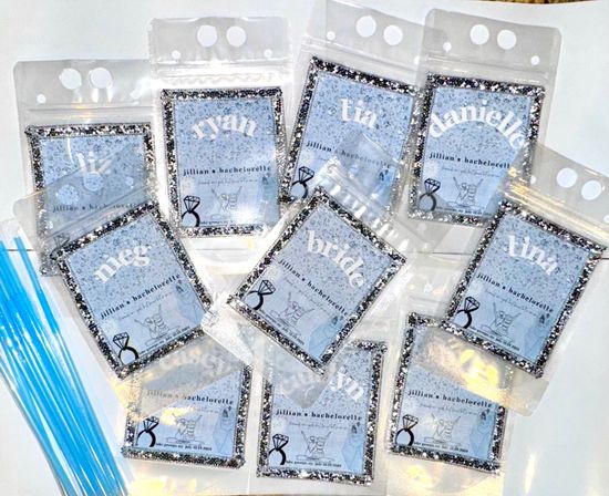 Sparkling silver-glitter framed personalized name pouches labeled for a bachelorette party with diamond ring icon and a bundle of blue drink straws on a white background