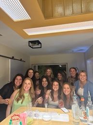 Smiling group of women gathered around a kitchen island with cocktails, bottles and snacks, enjoying a lively indoor house party.