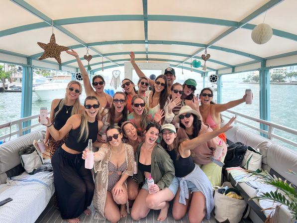 Energetic group of friends cheering and posing on a covered party boat cruising by a sunny marina waterfront