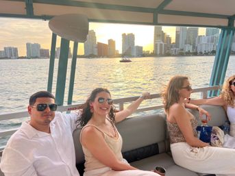 Group of friends lounging on a sunset boat cruise with Miami skyline and golden light reflecting on the bay.
