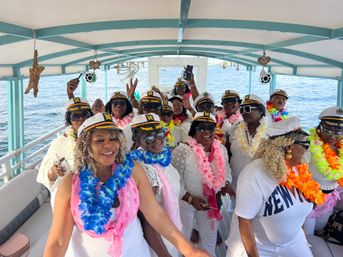Group of smiling women wearing captain hats and colorful leis on a covered party boat cruising on blue ocean water