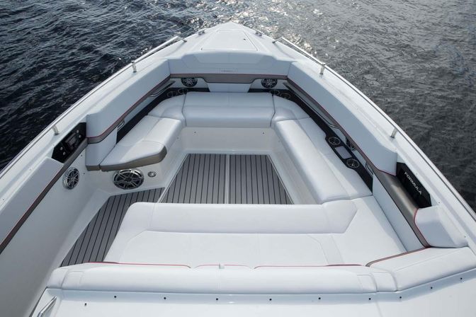Inviting white cushioned bow seating on a modern powerboat with gray striped deck, built-in marine speakers and cupholders, seen from above over dark rippling water.