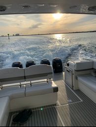 Golden sunset boat ride looking aft over four outboard engines and frothy wake, cushioned stern seating and deck with shoes, coastal skyline on the horizon.