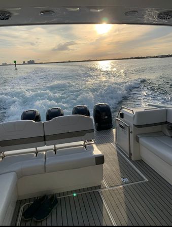 Golden sunset boat ride looking aft over four outboard engines and frothy wake, cushioned stern seating and deck with shoes, coastal skyline on the horizon.