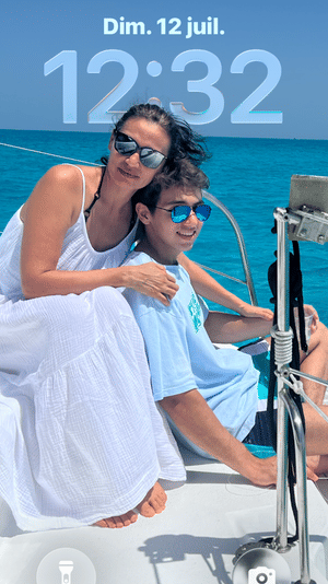 Mother and son in sunglasses smiling on a sailboat deck over clear turquoise ocean on a sunny summer sailing vacation.