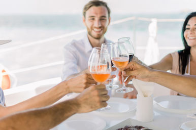 Smiling group toasting with rosé and red wine glasses on a sunny yacht deck with ocean in the background