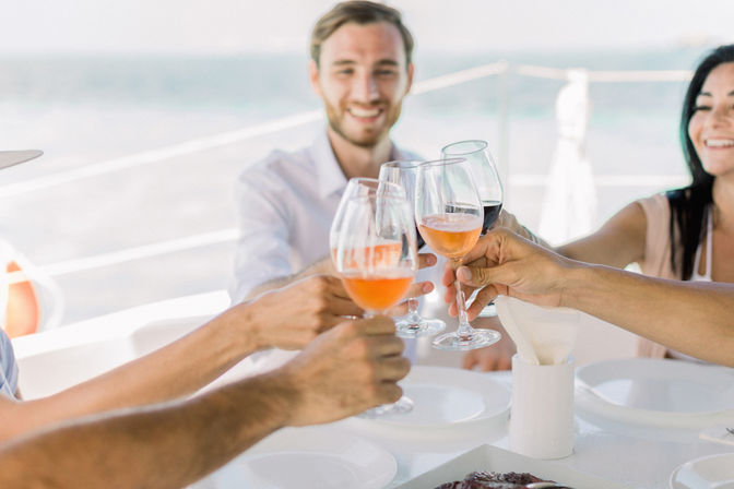 Smiling group toasting with rosé and red wine glasses on a sunny yacht deck with ocean in the background