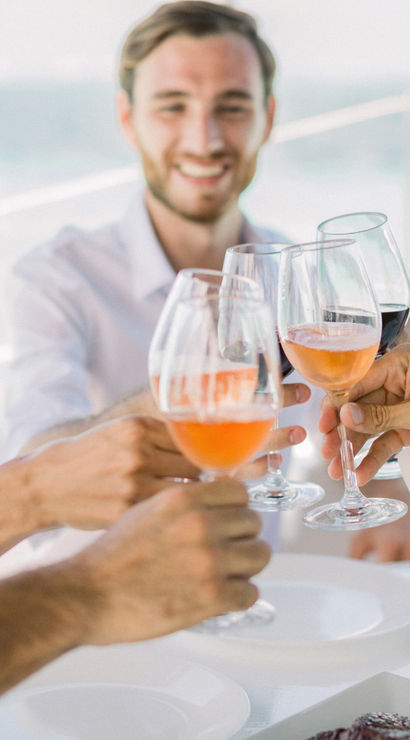 Smiling group toasting with rosé and red wine glasses on a sunny yacht deck with ocean in the background