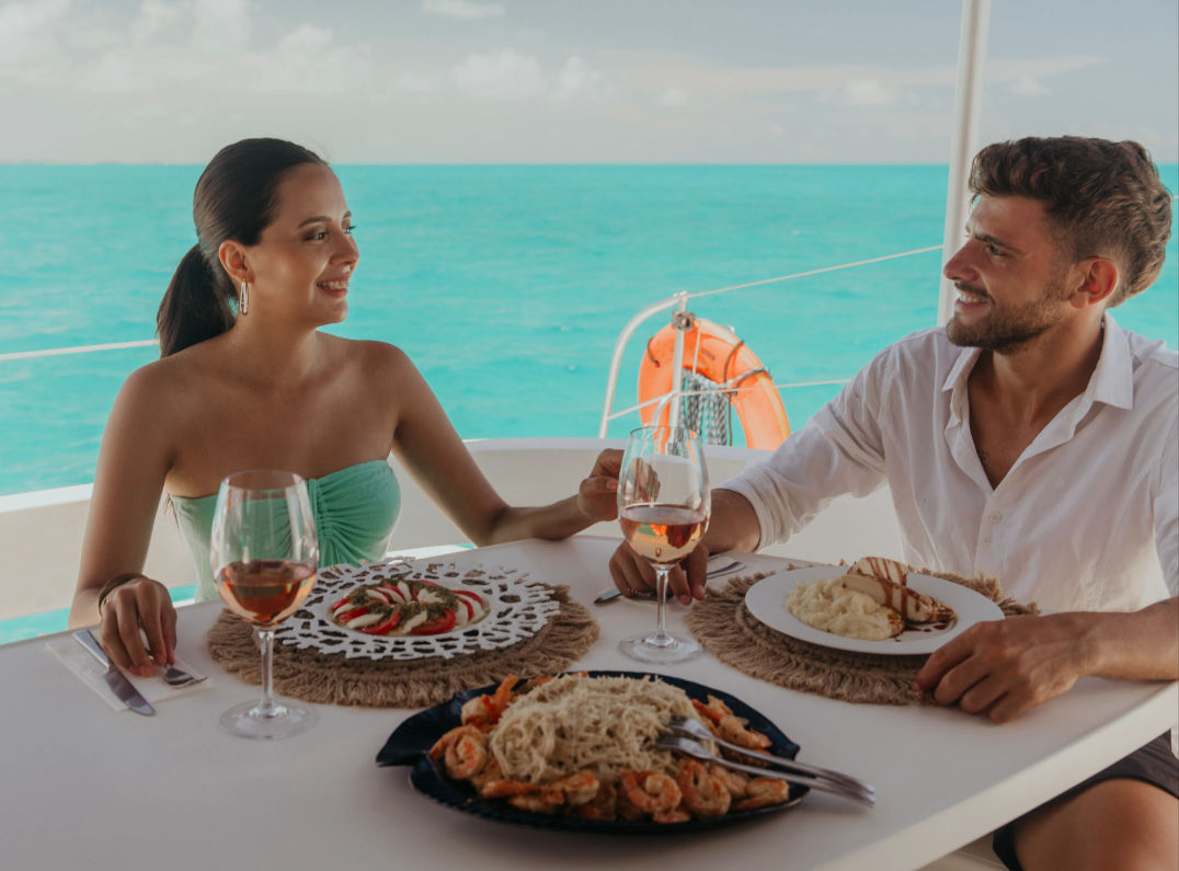 Couple enjoying a romantic seafood lunch and rosé wine on a yacht with turquoise ocean in the background.