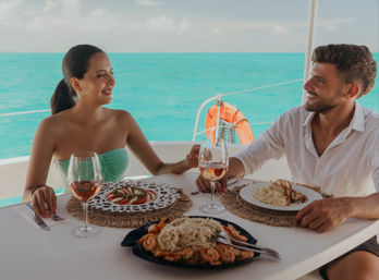 Couple enjoying a romantic seafood lunch and rosé wine on a yacht with turquoise ocean in the background.