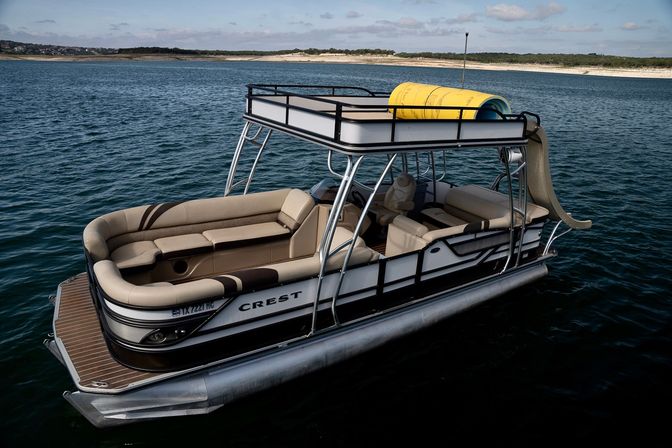 Pontoon boat on a calm lake with tan cushioned seating, a two-level canopy, a yellow inflatable tube on the roof and a waterslide ready for fun
