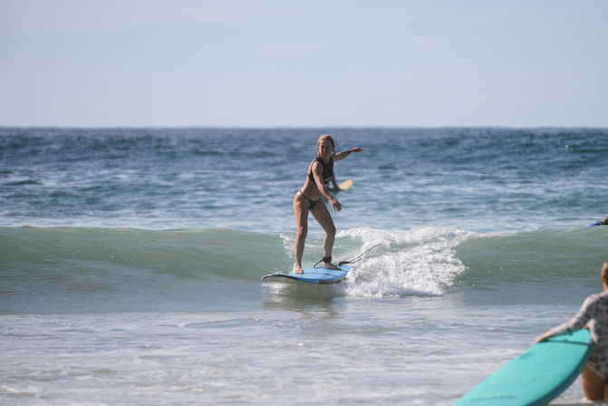 Surfer catching a gentle ocean wave on a blue surfboard near a sunny sandy beach.