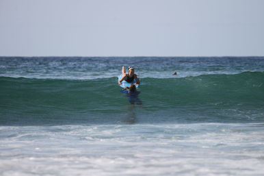 Surfer on a blue surfboard guided through a small green ocean wave, gentle beach surf and distant horizon