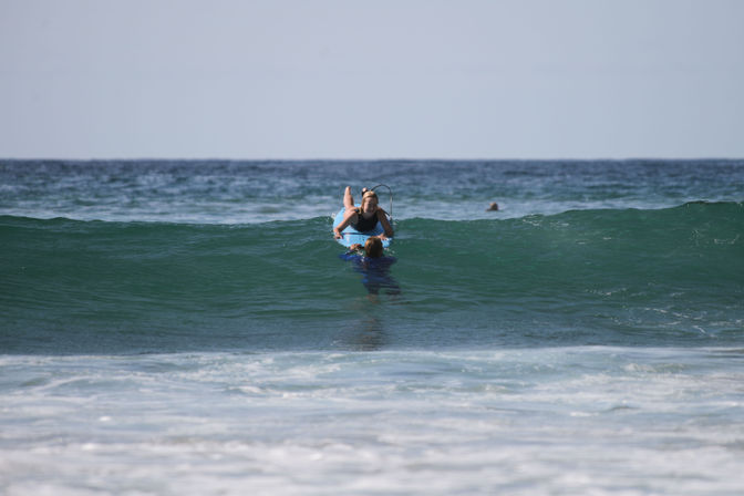Surfer on a blue surfboard guided through a small green ocean wave, gentle beach surf and distant horizon