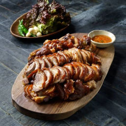 Sliced Korean-style braised pork hock (jokbal) on a wooden board with spicy dipping sauce, lettuce, garlic and green chilies for wraps