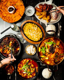 Overhead shot of a Korean feast: bubbling kimchi stew, spicy braises, corn cheese, kimchi pancake, fried chicken, rice and pickled radish