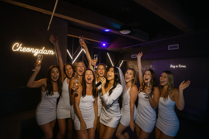 Bachelorette party at a karaoke bar — group of women in matching white dresses, bride-to-be wearing a veil singing and raising champagne flutes under neon lights