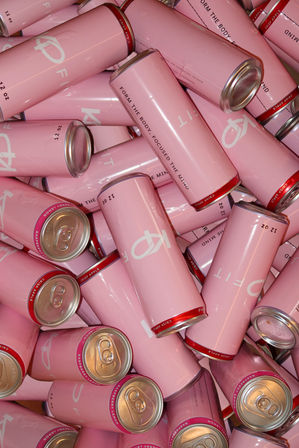 Close-up pile of pastel pink slim beverage cans with silver tops and red rims, overlapping in a colorful product display.